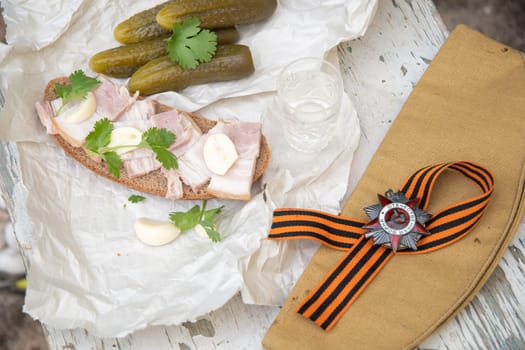 St. George's ribbon, Order of the Great Patriotic War, holiday May 9, Victory Day, still life on a shabby chair with glass of vodka and a snack of lard with garlic and pickled cucumber,
