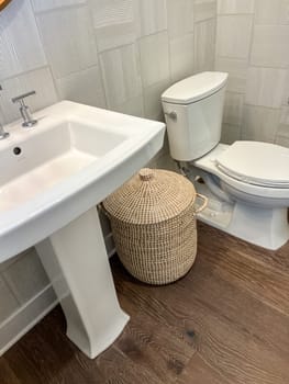 Castle Rock, Colorado, USA-May 14, 2023-A stylish powder room featuring a sleek pedestal sink and contemporary toilet against a textured wall. The wooden flooring adds warmth, while a woven basket provides functional decor. Perfect for compact spaces with a modern yet inviting design.