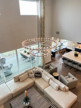 Castle Rock, Colorado, USA-May 14, 2023-Stunning open-concept living room and kitchen featuring a large sectional sofa, contemporary furniture, and an elegant crystal chandelier. The floor-to-ceiling windows provide ample natural light and a beautiful view of the patio and outdoor space. A perfect blend of modern design and cozy ambiance.