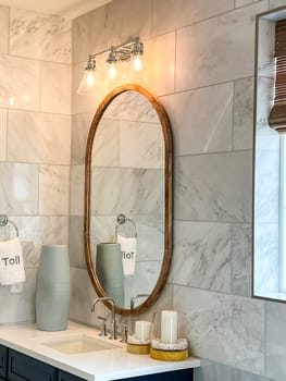 Castle Rock, Colorado, USA-May 14, 2023-Stylish bathroom vanity featuring a warm gold-framed mirror, triple-light fixture, and a luxurious marble countertop. The dark wood cabinetry adds contrast to the contemporary design, complemented by decorative accessories like textured vases and neatly placed towels. A perfect blend of function and elegance for a modern bathroom.