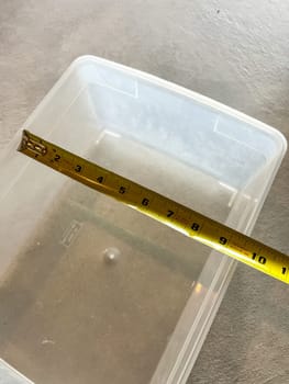 Castle Rock, Colorado, USA-May 29, 2023-A close-up image showing a yellow measuring tape inside a clear plastic container to determine its depth. The measurement reads approximately 2.5 inches. The container is placed on a smooth surface, highlighting its transparent design and functional use for storage or liquid measurements.
