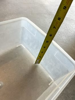 Castle Rock, Colorado, USA-May 29, 2023-A close-up image showing a yellow measuring tape inside a clear plastic container to determine its depth. The measurement reads approximately 2.5 inches. The container is placed on a smooth surface, highlighting its transparent design and functional use for storage or liquid measurements.