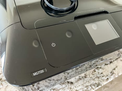 Castle Rock, Colorado, USA-May 8, 2023-A close-up image of a Canon printer placed on a granite countertop. The printer black glossy exterior prominently displays the Canon logo, reflecting light. The countertop beneath showcases a modern kitchen setting, blending functionality with sleek design.
