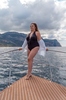 Woman on a yacht. Happy model in a swimsuit posing on a yacht against a blue sky with clouds and mountains.