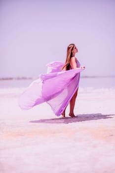 Woman pink salt lake. Against the backdrop of a pink salt lake, a woman in a long pink dress takes a leisurely stroll along the white, salty shore, capturing a wanderlust moment
