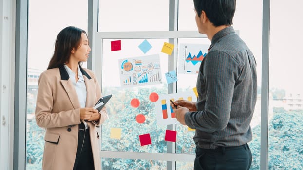 Business people work on project planning board in office and having conversation with coworker friend to analyze project development . They use sticky notes posted on glass to make it organized. Jivy