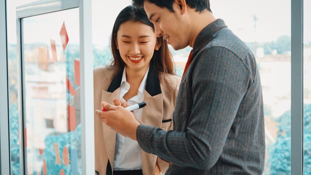 Business people work on project planning board in office and having conversation with coworker friend to analyze project development . They use sticky notes posted on glass to make it organized. Jivy