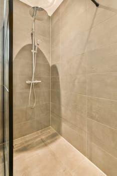 a shower room with tile flooring and gray tiles on the walls, there is an overhead shower head mounted in the wall