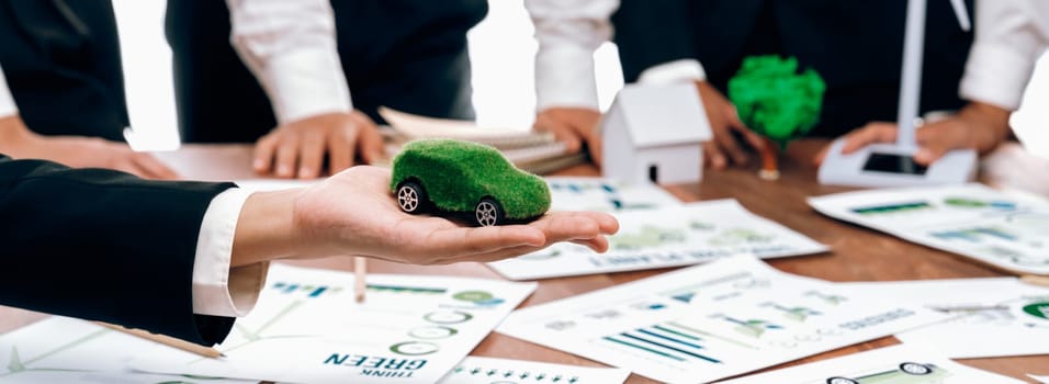 Businessman holding green EV car model mock in electric car company meeting, business people planning strategic marketing for eco-friendly vehicle product using clean energy with net zero.Trailblazing