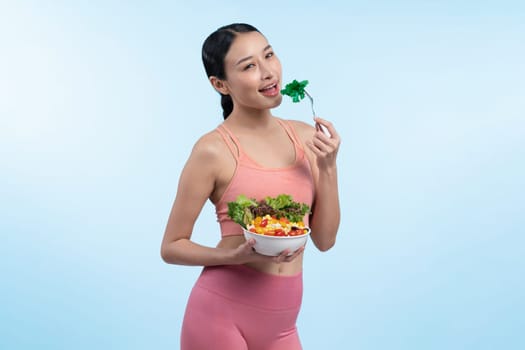 Young sporty Asian woman in sportswear holding salad bowl fill with vibrant of fruit and vegetable. Natural youthful and fit body lifestyle with balance nutrition on isolated background. Vigorous