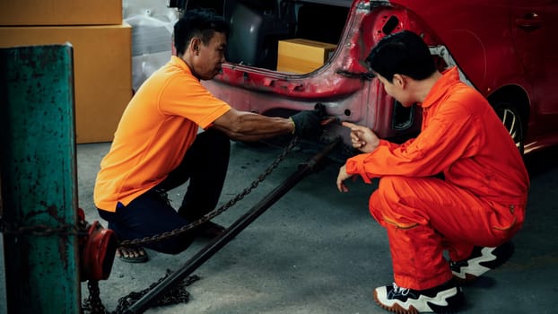 Mechanic testing strength and reliability of chain hoist for car towing in car workshop garage. Automotive service worker ensure through inspection of mechanical equipment. Oxus