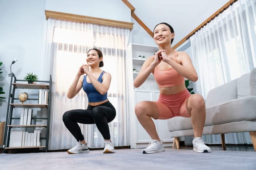 Vigorous energetic woman with trainer or workout buddy doing exercise at home. Young athletic asian woman strength and endurance training session as home workout routine with squat.