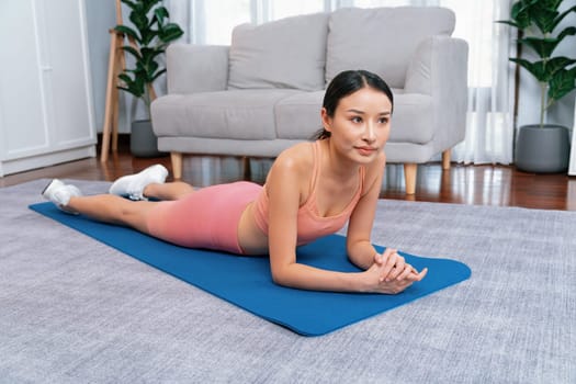 Young attractive asian woman in sportswear lying down or reclining on exercise mat. Home exercising and workout routine on the floor. Vigorous