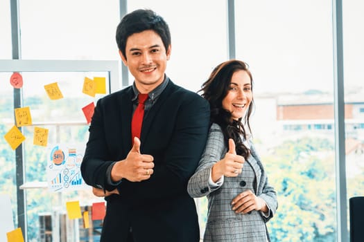 Two happy businesspeople holding thumbs up in modern office . Jivy