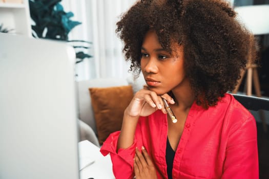 African american businesswoman creating project job's customer on computer with standing on desk at home office, writing crucial information on the paper. Concept of creative working life. Tastemaker.