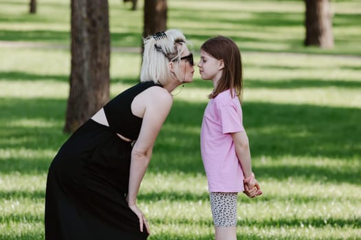 Girl kisses mother in spring or summer park. Family relaxing outdoors. Mothers day. Close up.