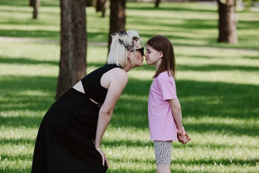 Girl kisses mother in spring or summer park. Family relaxing outdoors. Mothers day. Close up.