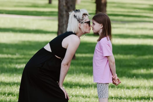 Girl kisses mother in spring or summer park. Family relaxing outdoors. Mothers day. Close up.