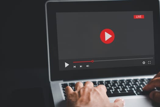 A man engrossed in his laptop screen, seamlessly switching between a video player and online training, embodying the concept of telework and e-learning from the comfort of home.