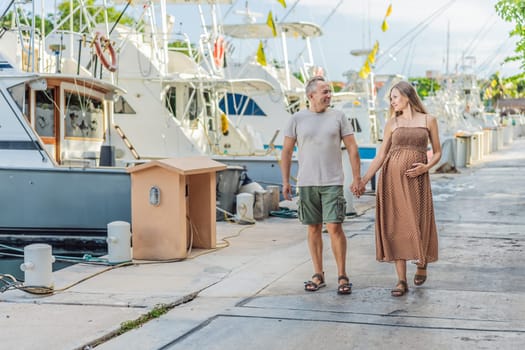 A happy, mature couple over 40, enjoying a leisurely walk on the waterfront, their joy evident as they embrace the journey of pregnancy later in life.