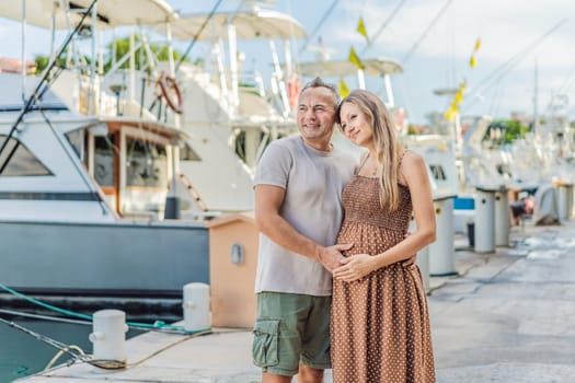 A happy, mature couple over 40, enjoying a leisurely walk on the waterfront, their joy evident as they embrace the journey of pregnancy later in life.