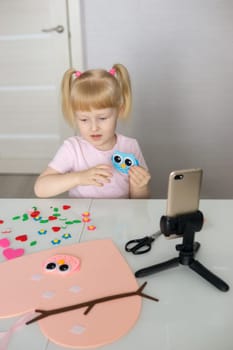 A blogger girl makes a felt craft for Valentine's Day in the shape of a heart. The concept of children's creativity and handmade.