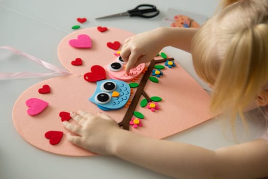 A blogger girl makes a felt craft for Valentine's Day in the shape of a heart. The concept of children's creativity and handmade.