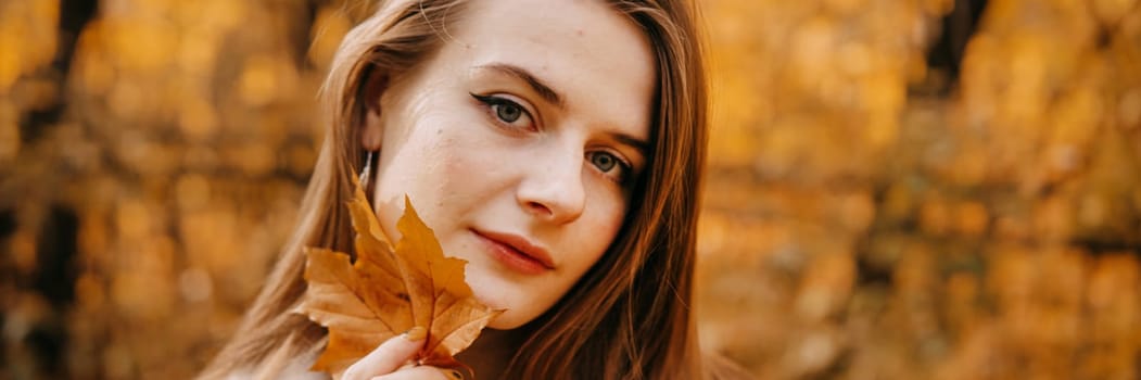 Portrait of a woman with an autumn maple leaf. Railway, autumn leaves, a young long-haired woman in a light coat coat, close-up.