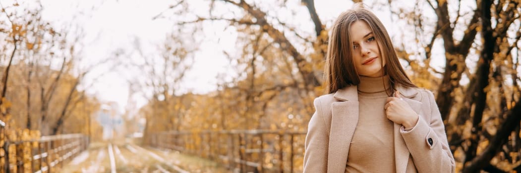 A beautiful long-haired woman walks through the autumn streets. Railway, autumn leaves, a woman in a light coat.