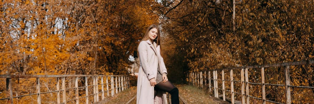 A beautiful long-haired woman walks through the autumn streets. Railway, autumn leaves, a woman in a light coat.