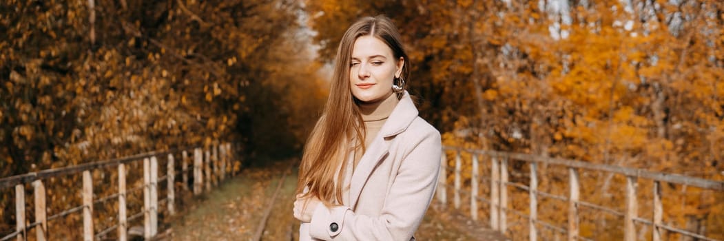 A beautiful long-haired woman walks through the autumn streets. Railway, autumn leaves, a woman in a light coat.