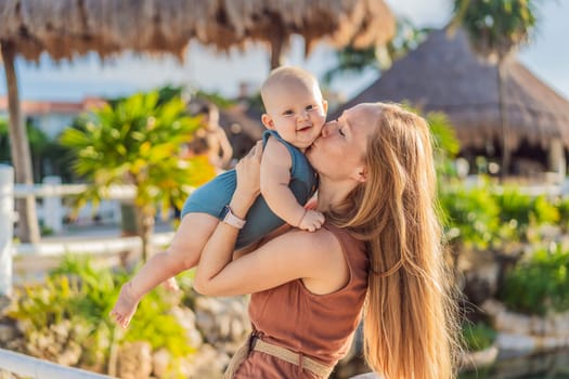 Amidst tropical palms and thatched roofs, a loving mom embraces her baby, sharing warmth and affection in a tranquil outdoor setting.