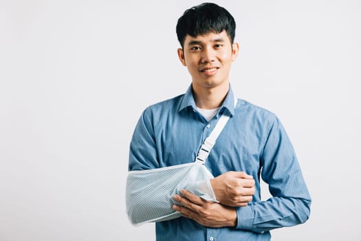 Injured businessman remains confident while dealing with broken arm, utilizing splint for treatment. happy Asian man in sling for support, on white background, signifying path to recovery. Copy space