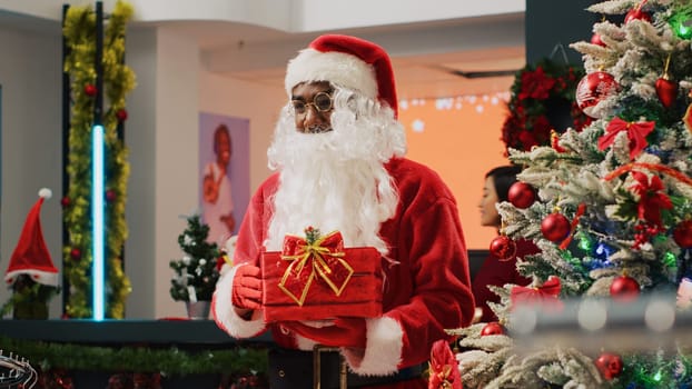 Elderly couple in xmas decorated clothing store giving raffle ticket to worker dressed as Santa Claus holding gift acting as collecting box. Employee organising Christmas promotion event