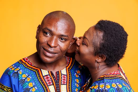 African american man and woman couple sharing secret, expressing love and affection. Black woman whispering to husband ear, telling private romantic message on studio background