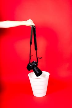 Hand with old digital camera in a trash can, isolated on red background