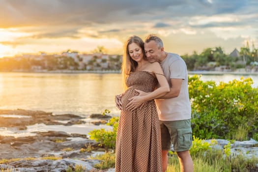 A happy, mature couple over 40, enjoying a leisurely walk on the waterfront On the Sunset, their joy evident as they embrace the journey of pregnancy later in life.