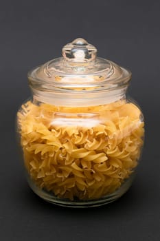 Uncooked Fusilli Pasta in Glass Jar on Black Background. Raw and Dry Macaroni. Unhealthy and Fat Food. Italian Culture