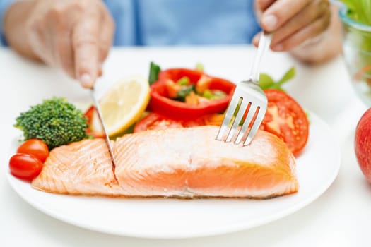 Asian elderly woman patient eating salmon stake and vegetable salad for healthy food in hospital.