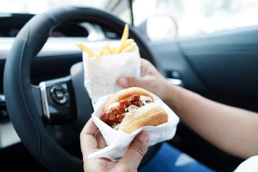 Asian woman driver hold and eat hamburger and french fries in car, dangerous and risk an accident.