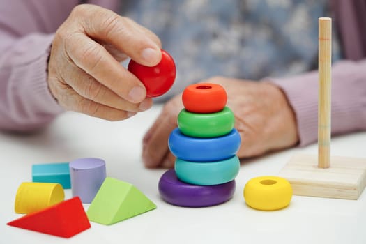 Bangkok, Thailand - May 15, 2022 Asian elderly woman playing Rubik cube game to practice brain training for help dementia prevention and Alzheimer disease.