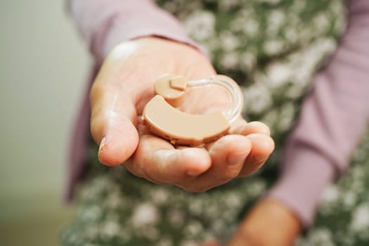 Asian senior woman patient using hearing aid in ear to reduce hearing loss problem.