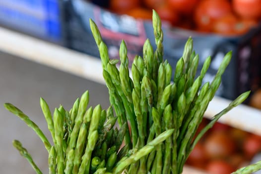 A bunch of fresh asparagus stands out against a colorful backdrop of ripe tomatoes at a lively market.