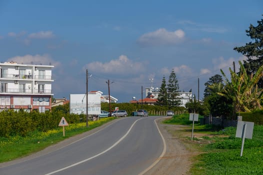 A winding road surrounded by vibrant greenery leads toward a distant harbor under a clear blue sky.