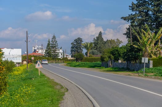 A peaceful drive unfolds next to vibrant greenery and modest buildings under a bright blue sky with soft clouds.
