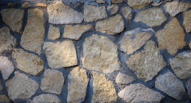 Roughly shaped stones blend harmoniously in a textured wall illuminated by warm afternoon rays.