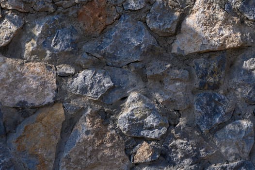 A diverse arrangement of rough stones forms a sturdy wall, illuminated by soft daylight revealing unique textures.