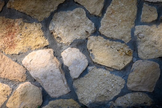 Sunlight highlights the diverse shapes and hues of a rustic stone wall, showcasing its natural beauty and craftsmanship.
