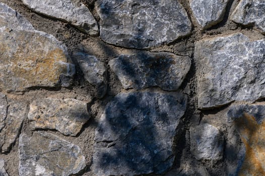 Sunlight spills across the rough stones, showcasing the intricate textures and tranquil beauty of this natural wall.