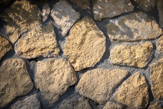 Sunlight filters through trees, illuminating the textured surface of a rustic stone wall, enhancing the natural beauty.